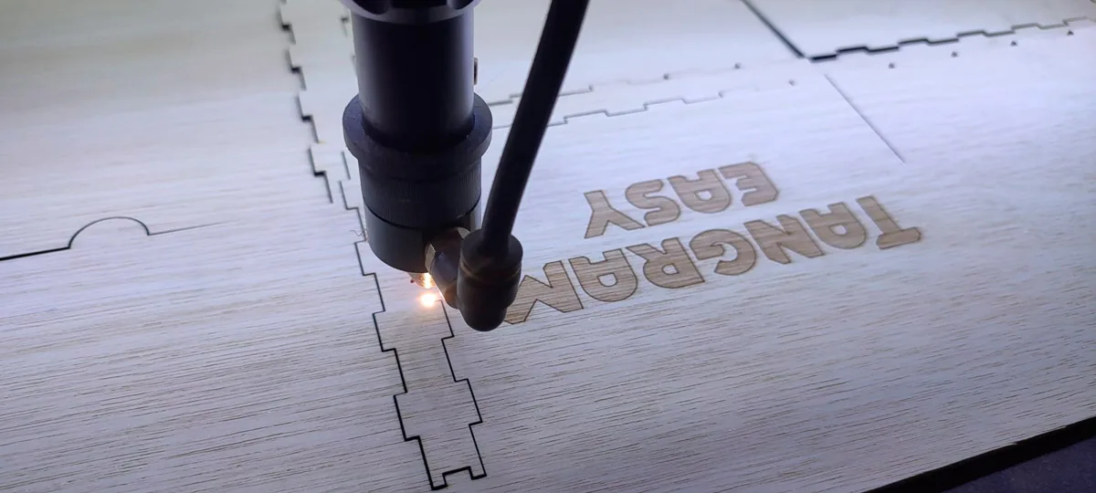 Laser head cutting and engraving the Tangram Easy logo on plywood